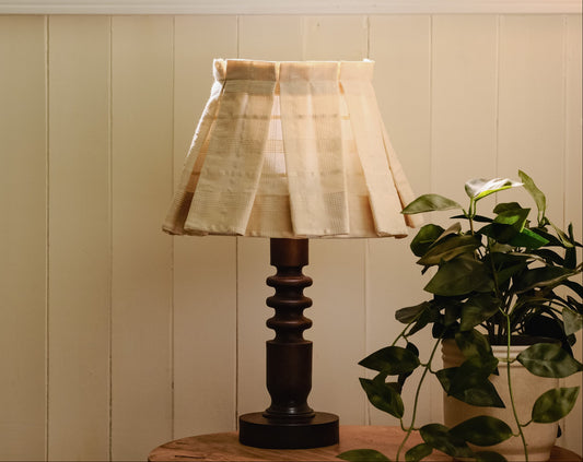 Table lamp with a cream decorative shade on a wooden surface next to a plant against a beige wall.