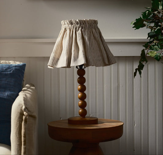 Wooden lamp with a scrunchie stripped shade on a wooden base against a white paneled wall.