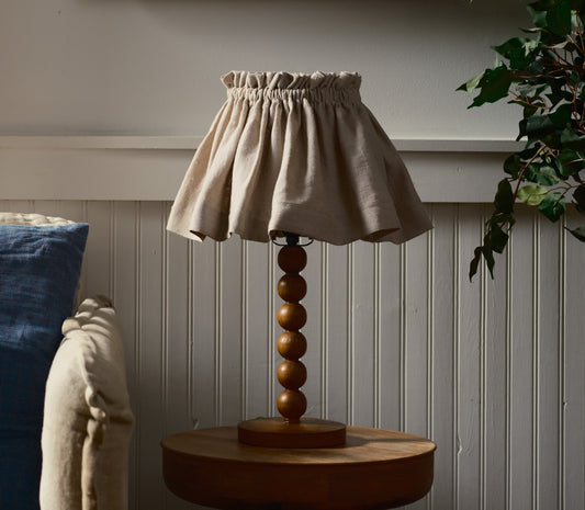 Decorative lamp with a beige shade and wooden base on a table against a wall.