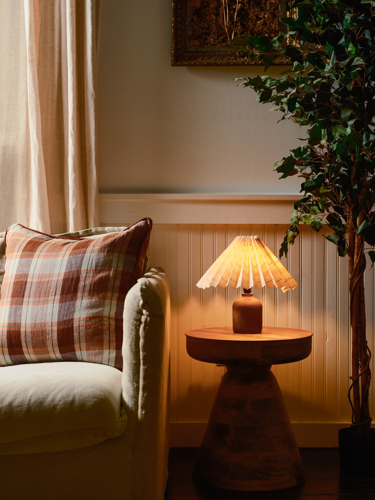 Cozy living room corner with a plaid pillow, lamp, and plant.