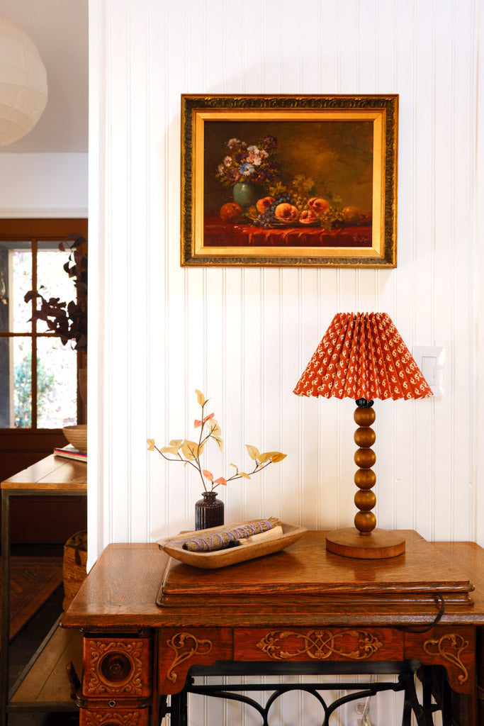 floral lampshade and decorative items on a table with a painting in the background. 