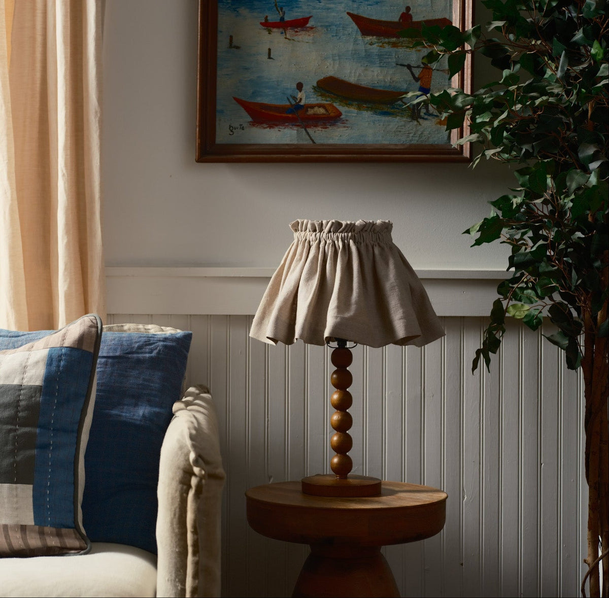 lampshade on a pedestal table with couch and painting in background 