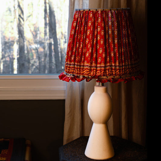 Lamp with a red patterned shade in a room with a window and curtains.