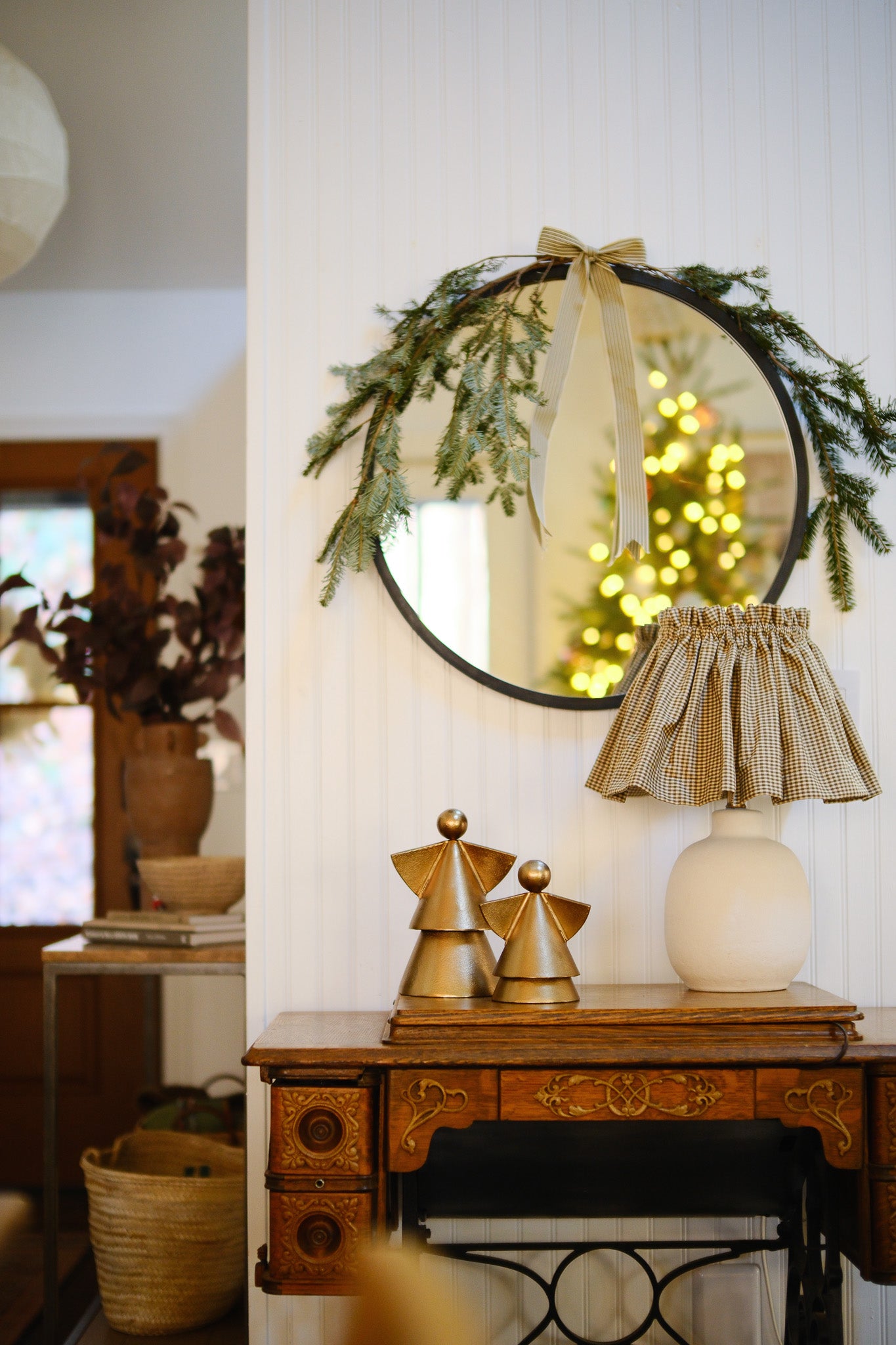 Decorative mirror with greenery, lamp, and sculptures on a wooden table.