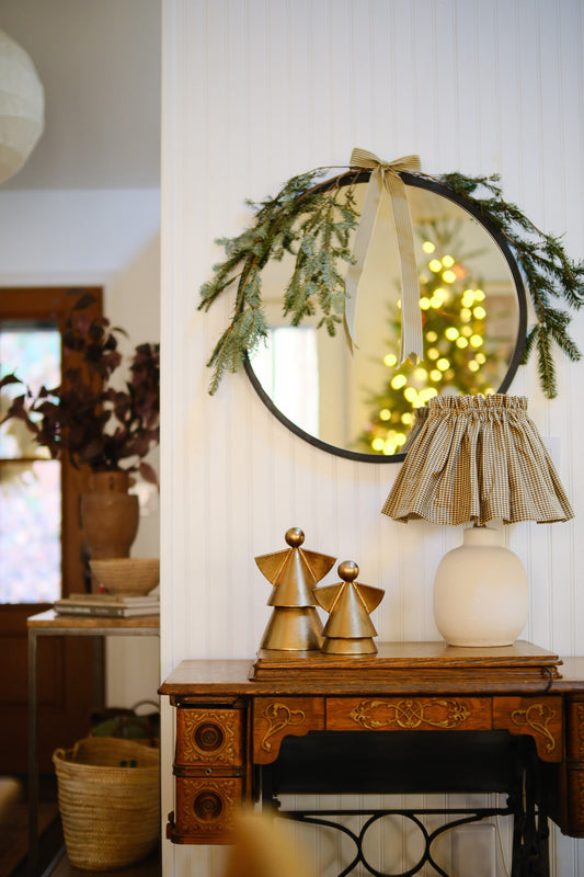 Decorative mirror with greenery, lamp, and sculptures on a wooden table.