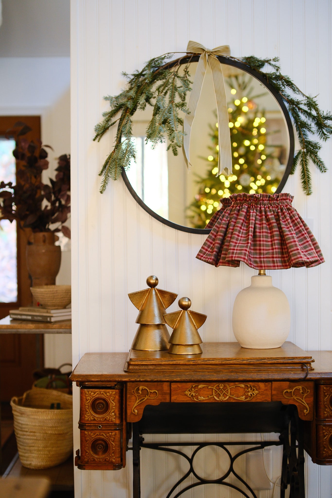 Decorative mirror with greenery and a plaid skirt, gold figurines on a wooden table.
