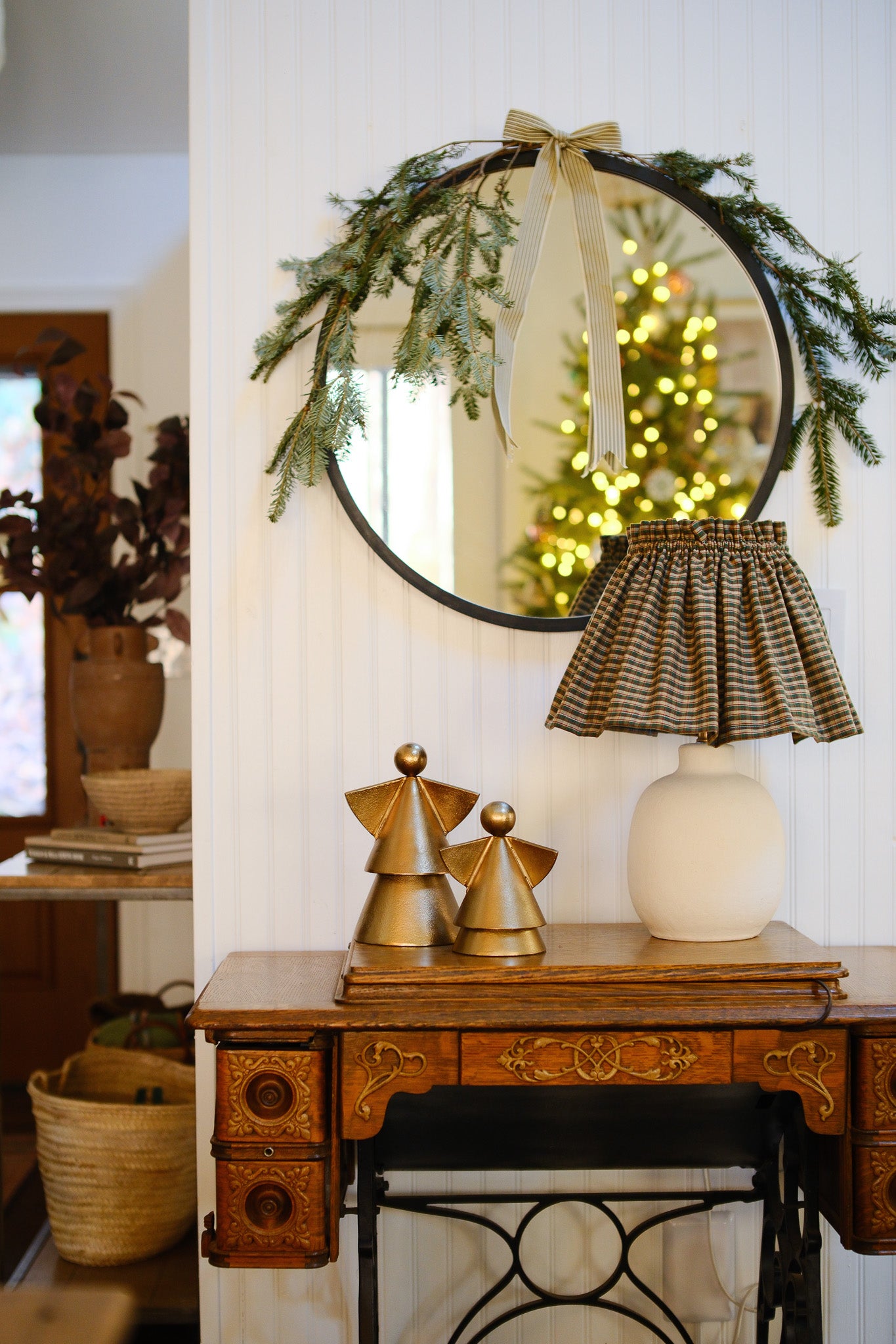 Decorative mirror with greenery and a lamp on a wooden table.