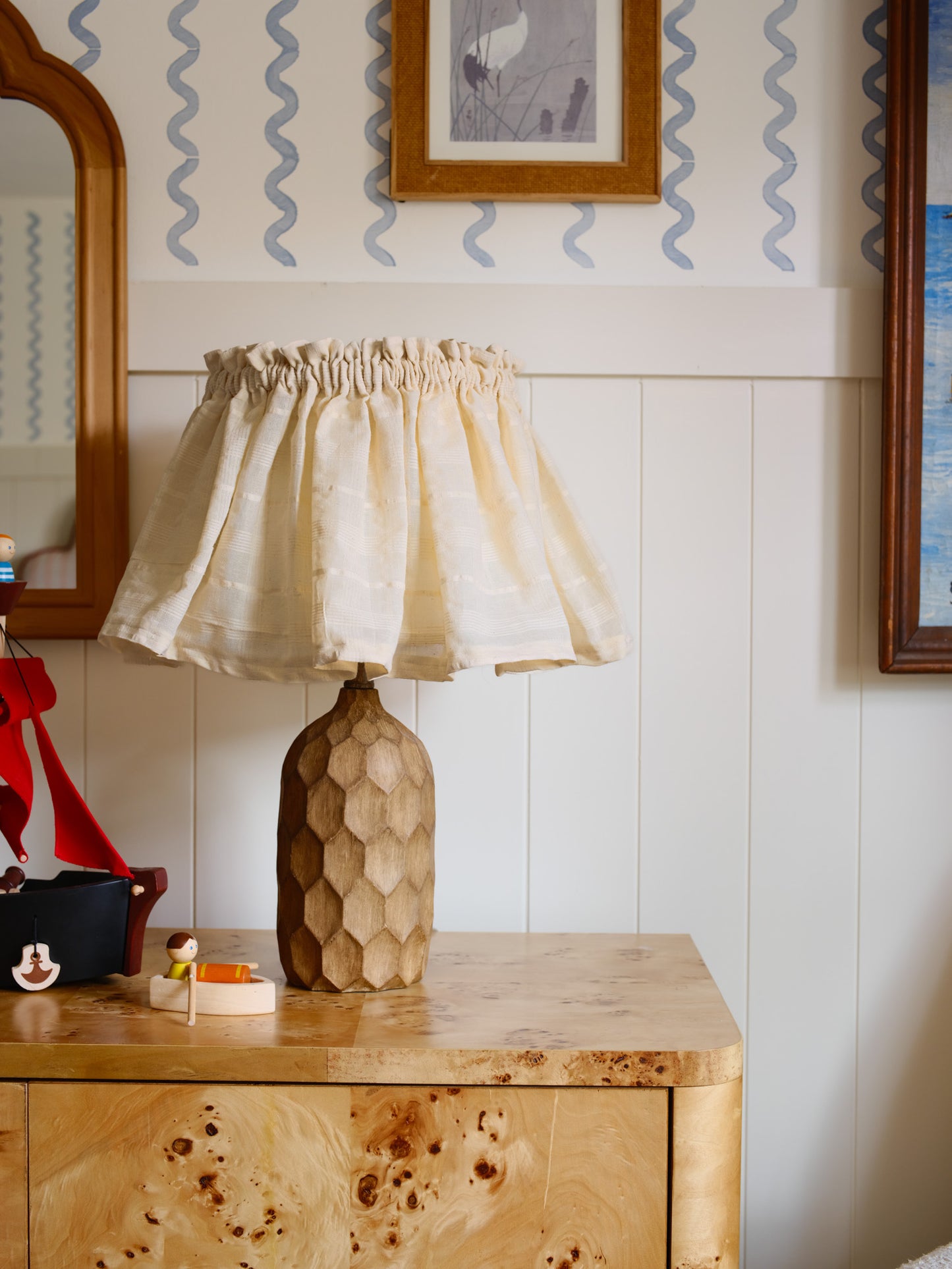 Beige lamp with a textured base on a wooden surface against a wall with wavy pattern