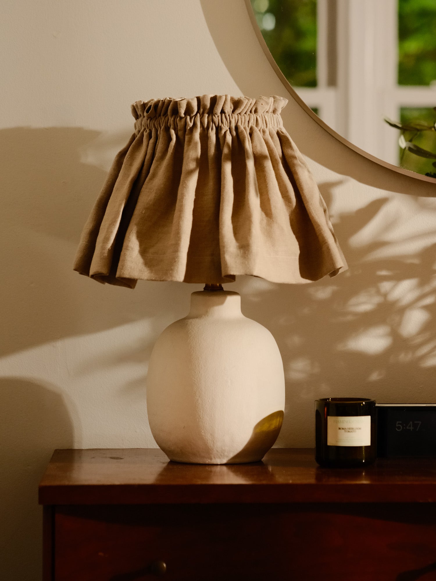Lamp with a brown fabric shade on a wooden surface, with a mirror and candle in the background.