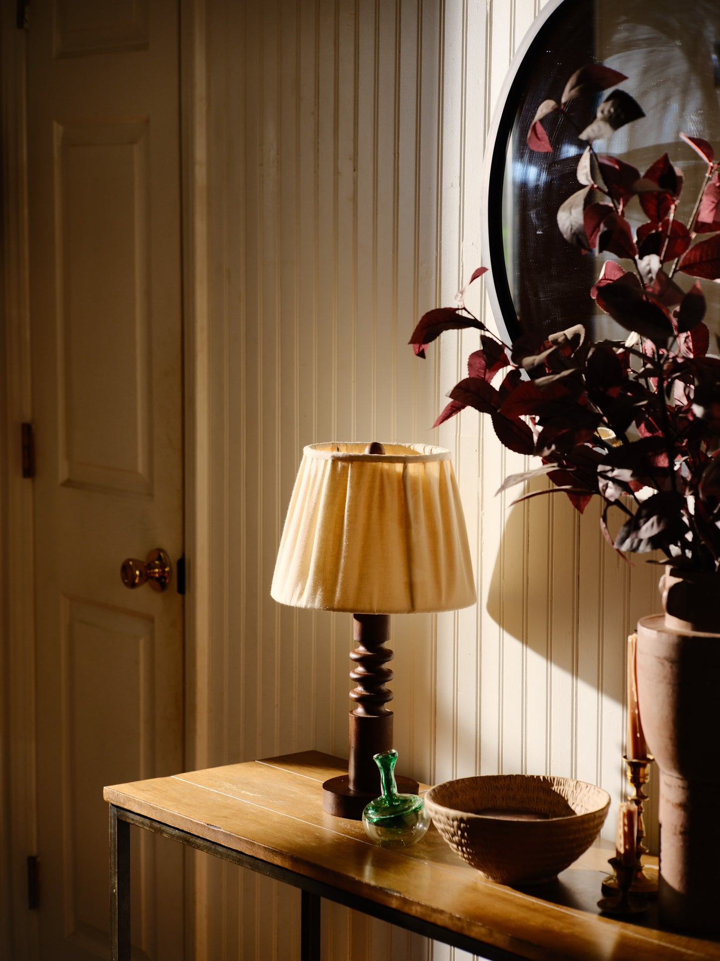 Wooden table with a lamp, decorative bowl, and plant against a neutral wall.