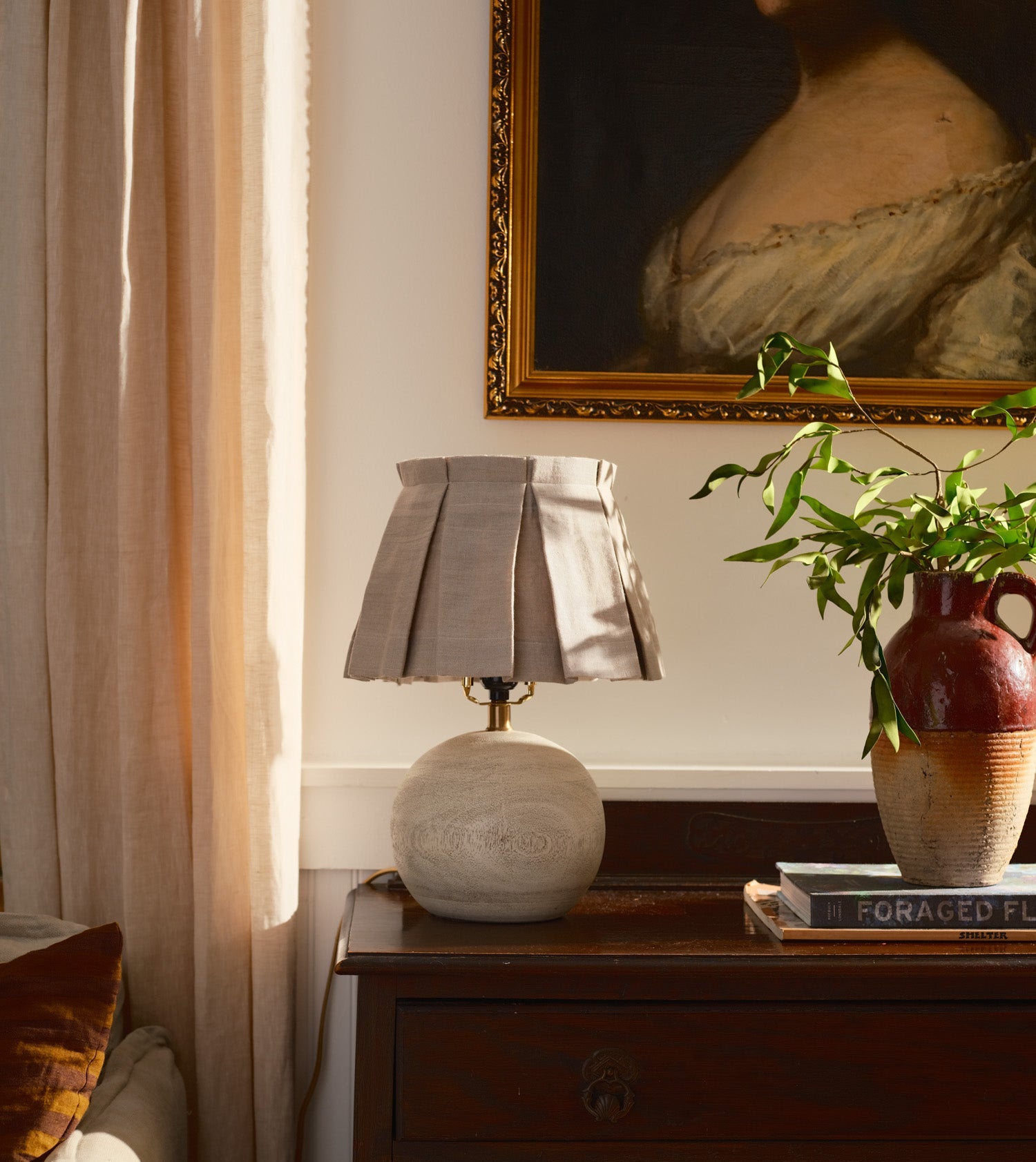 Lamp with a beige box pleated lampshade on a wooden nightstand.