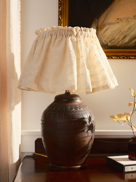 Decorative lamp with a textured base and white lampshade on a wooden surface.