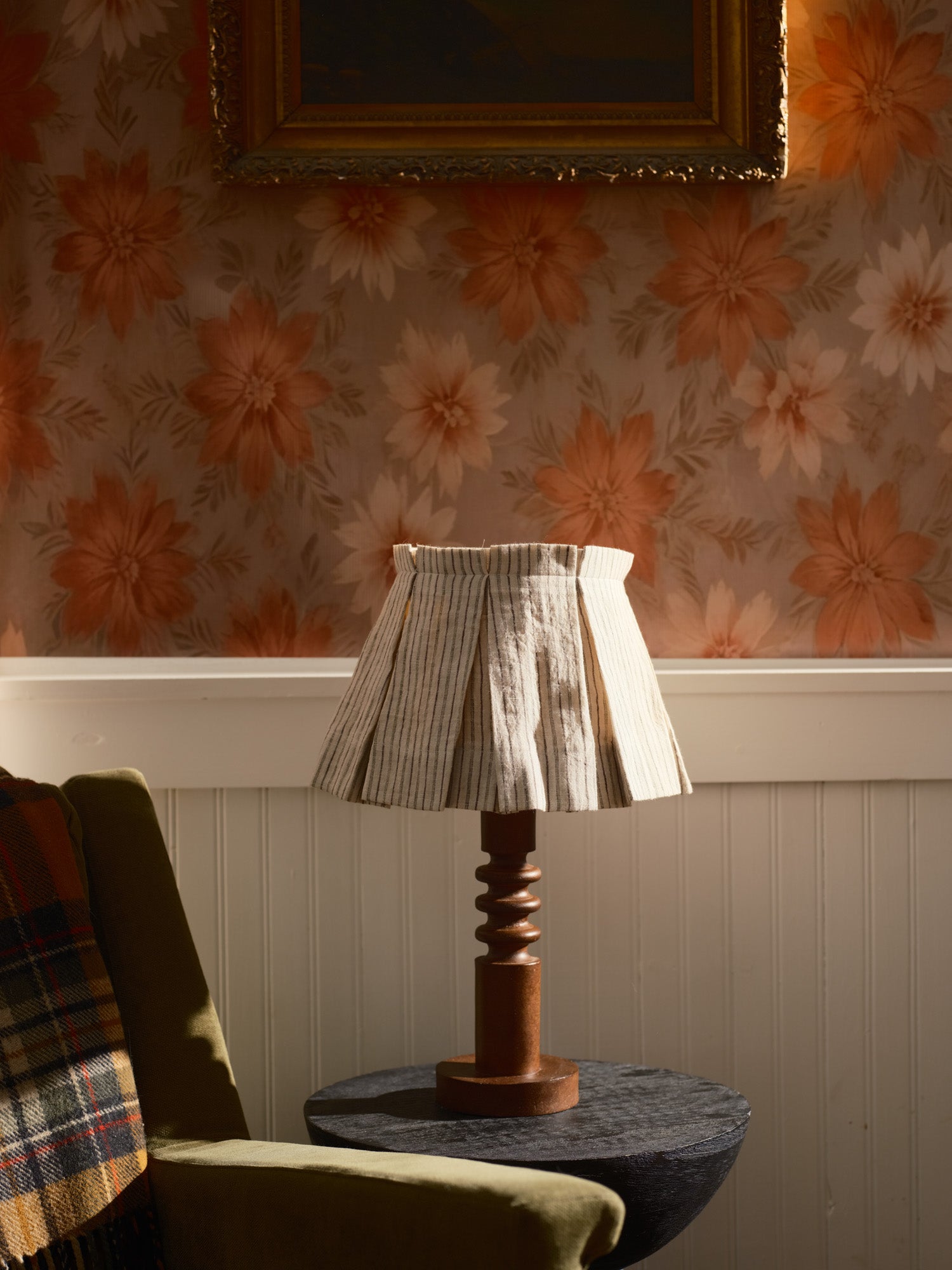Lamp on a table with floral wallpaper and a framed picture in the background