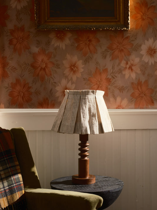 Lamp on a table with floral wallpaper and a framed picture in the background