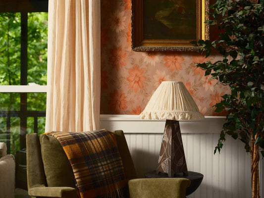 Living room with a green armchair, plaid blanket, lamp, and floral wallpaper.