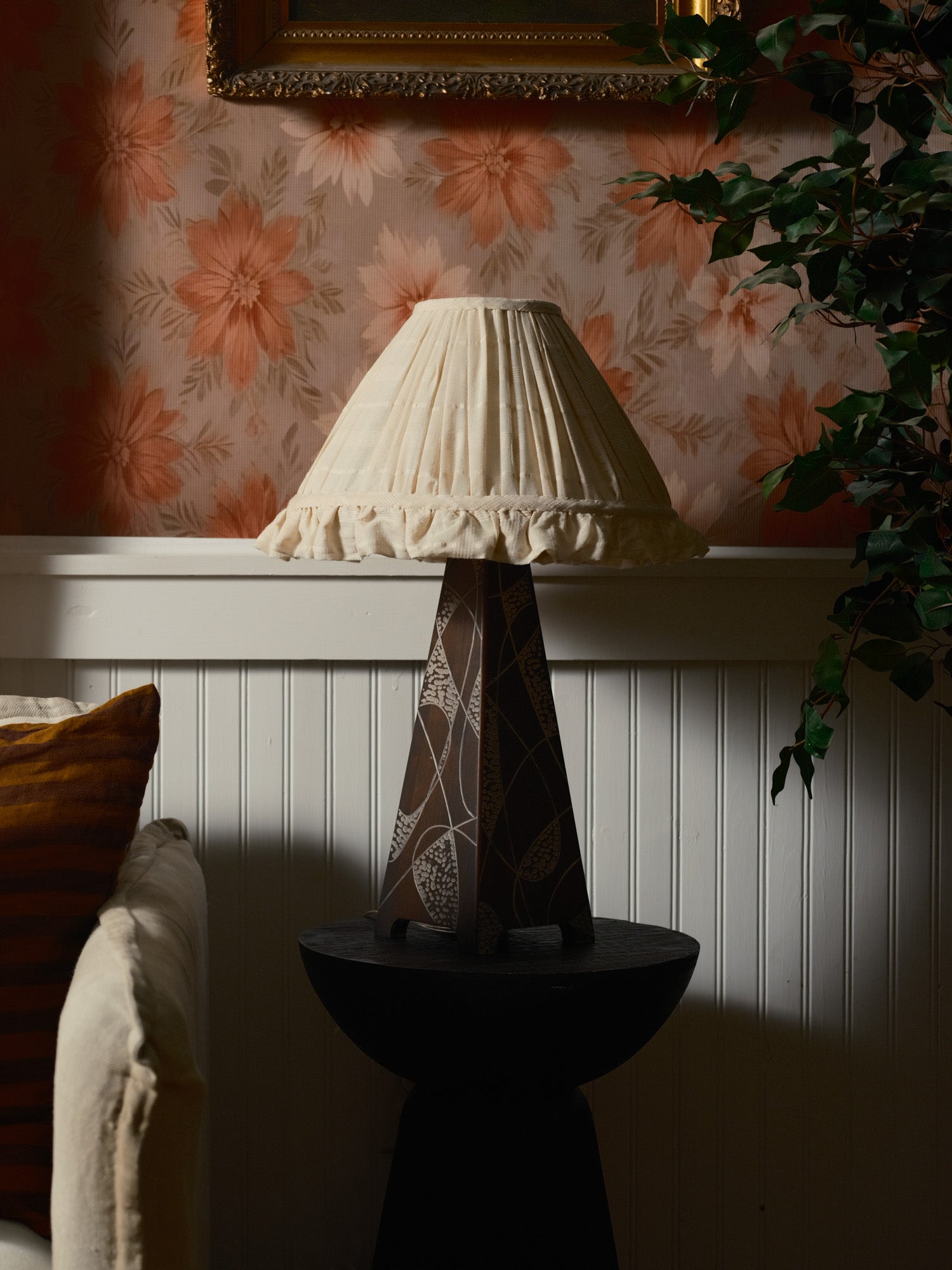Decorative lamp with a patterned shade on a pedestal against floral wallpaper.