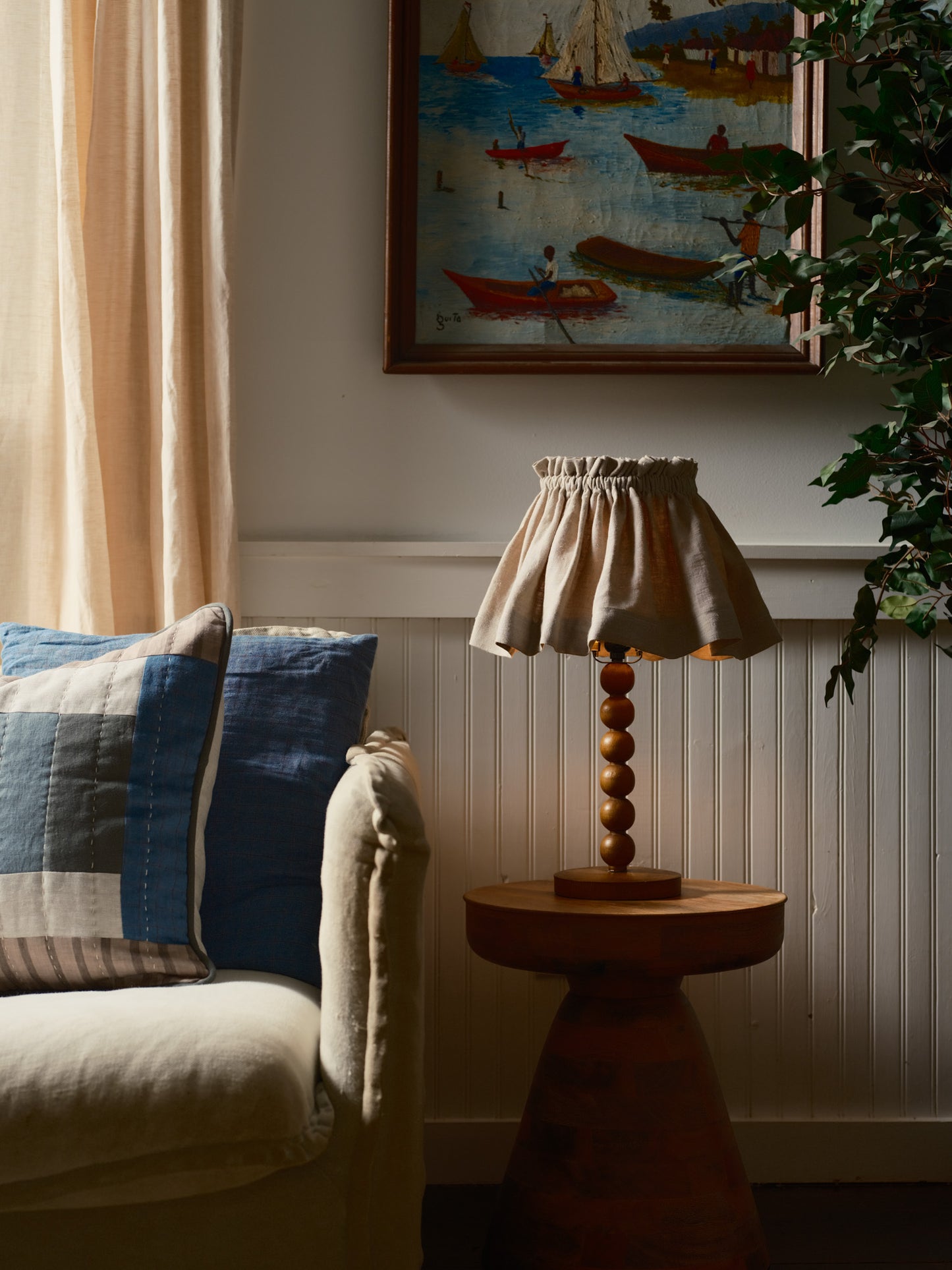 Living room with a lamp on a side table, sofa with cushions, and wall art.