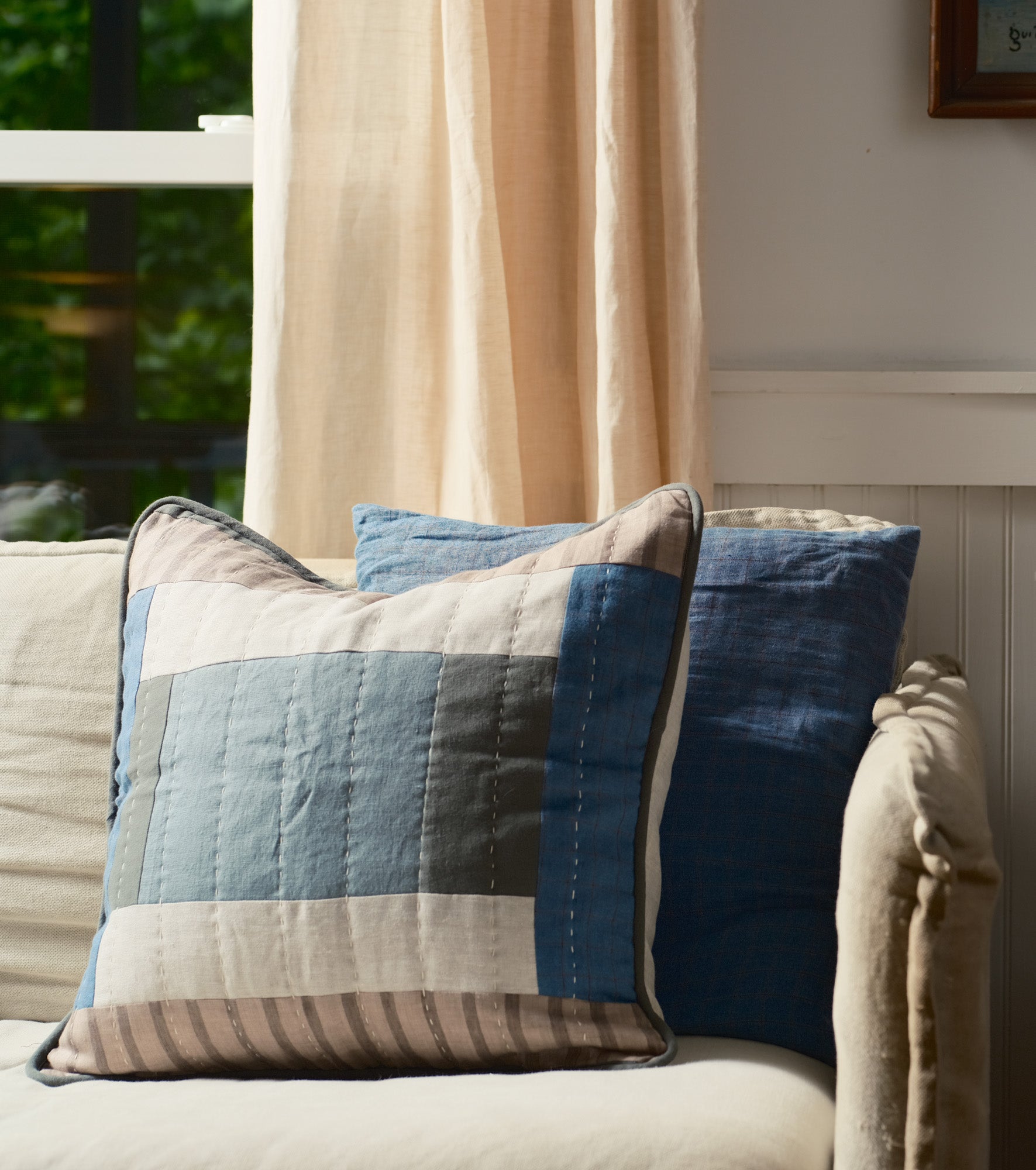 Blue Patchwork Decorative pillow on a sofa with a neutral curtain in the background