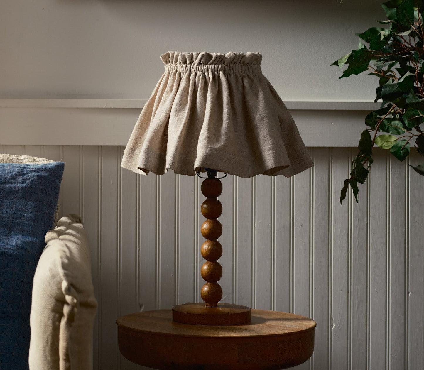 Decorative lamp with a beige shade and wooden base on a table against a wall.