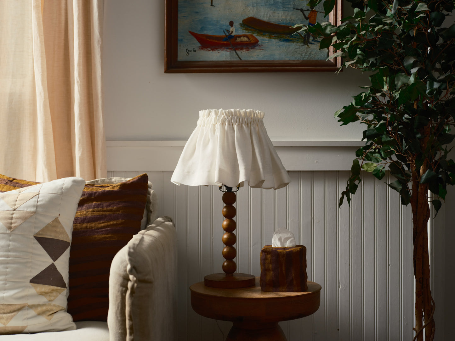 Lamp on a side table with a painting and plant in the background