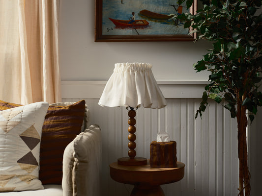 Lamp on a side table with a painting and plant in the background