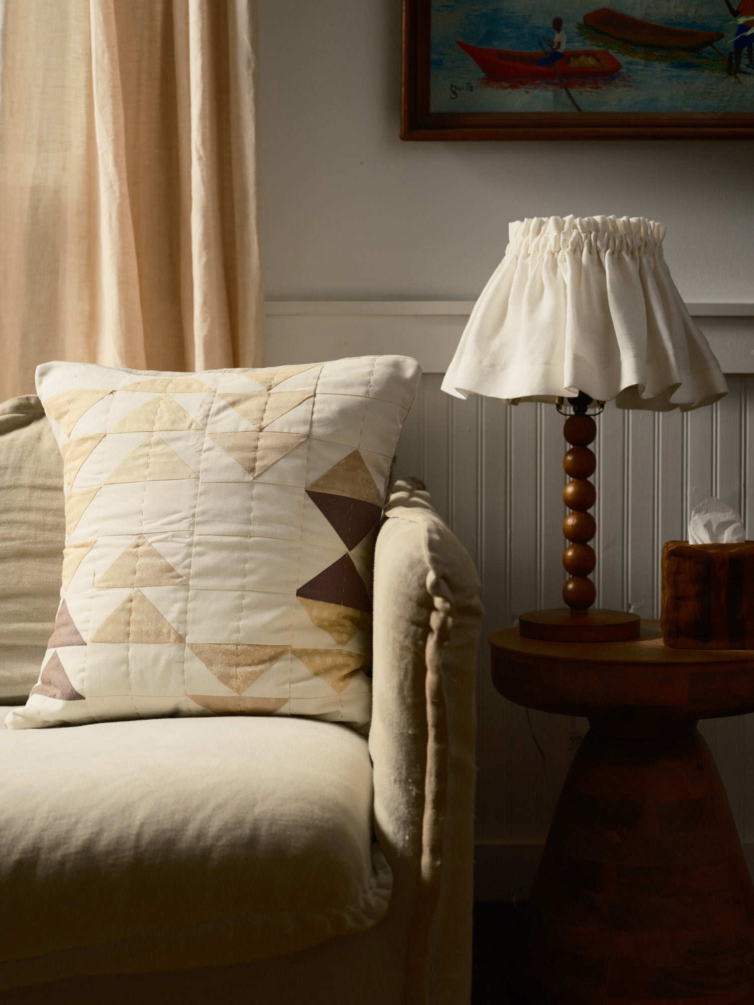 Living room with beige sofa, patterned pillow, wooden lamp, and framed artwork.
