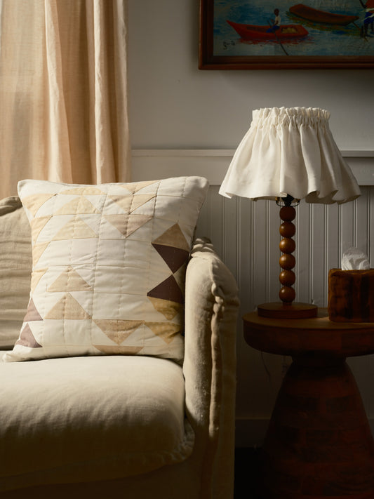 Living room with beige sofa, patterned pillow, wooden lamp, and framed artwork.