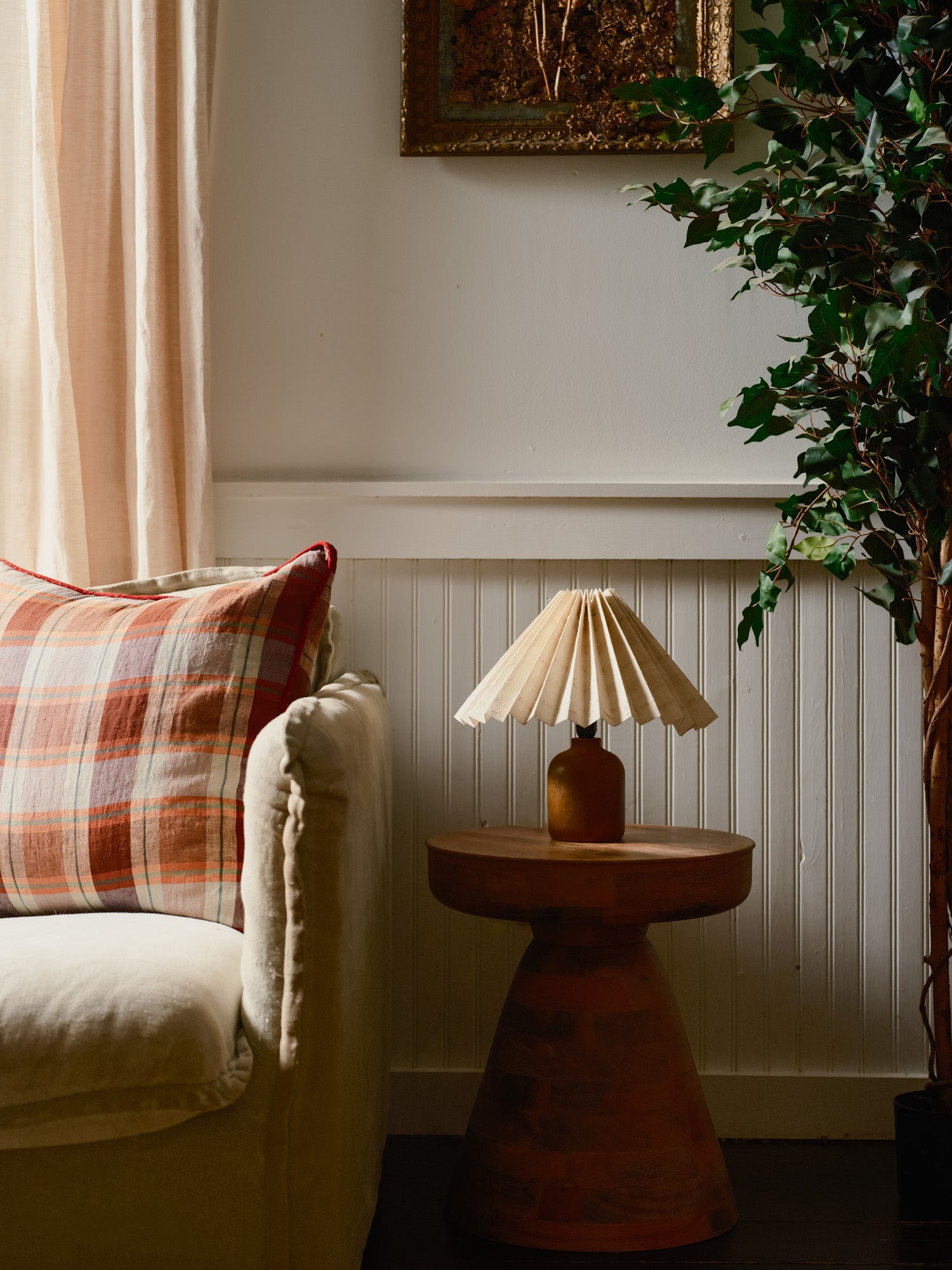 Cozy living room corner with a lamp on a small table, plaid pillow, and plant.